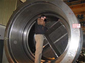 Engineer standing inside the shell of a large-diameter heat exchanger beside its tubesheet