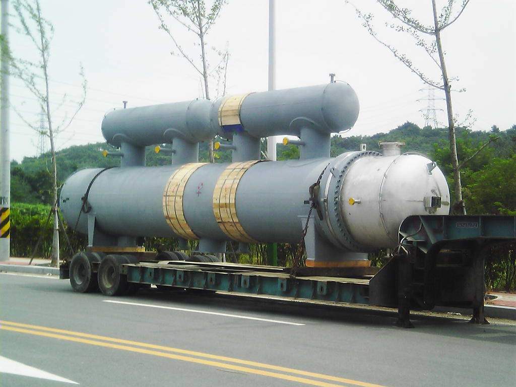 Large shell-and-tube heat exchanger with stacked separator drums on a lowboy trailer, en route to site